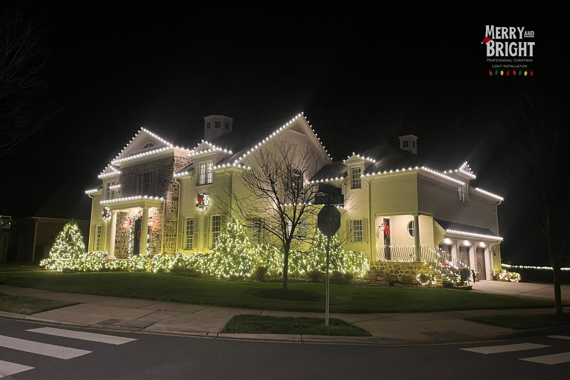 Layered warm white rooflines, wreaths, and illuminated landscaping on a Davidson home